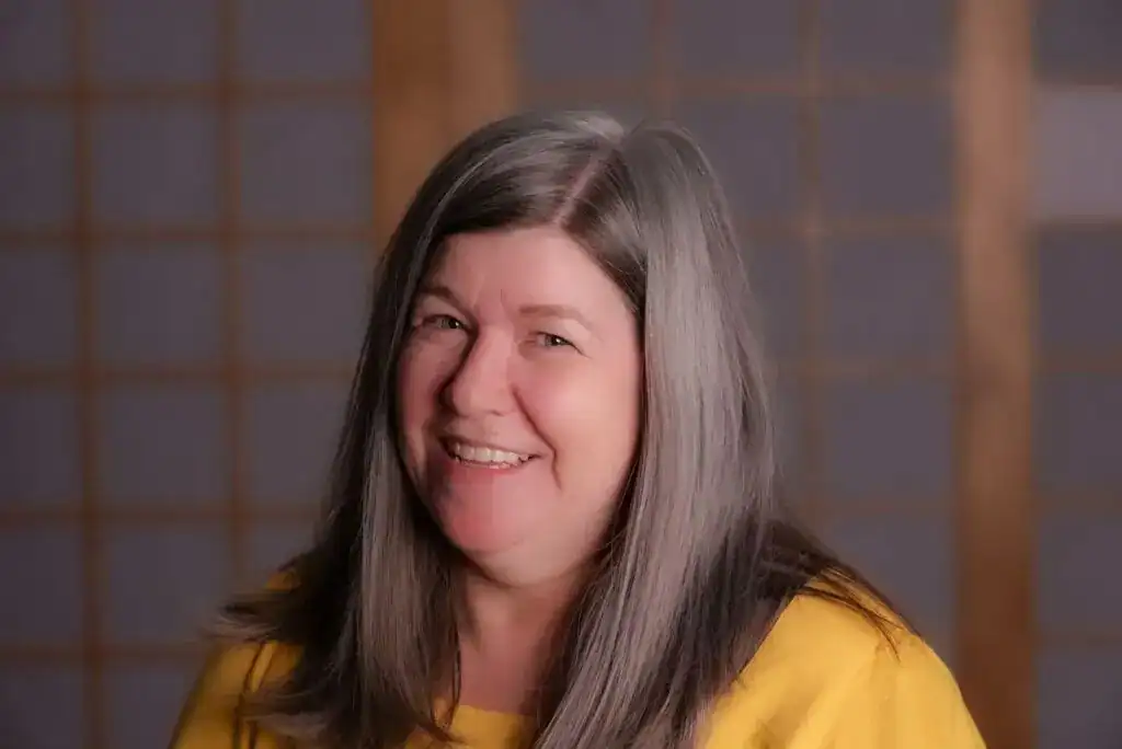 Smiling woman with long gray hair in front of traditional Japanese shoji screen, representing Kamloops Japanese Canadian Cultural Centre.